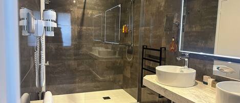 A modern bathroom with a glass-enclosed shower, a large mirror, and a marble countertop.