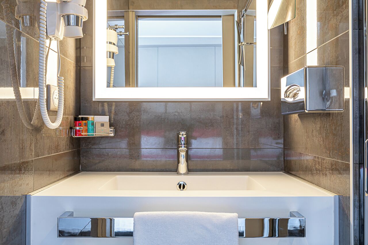 Un baño moderno con un espejo grande, un lavamanos y una ducha.