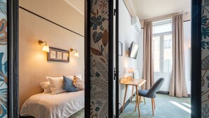 A bedroom with a bed, bedside table, lamp, and a view of the outside through a window. - La Maison d'été (Salon-de-Provence)