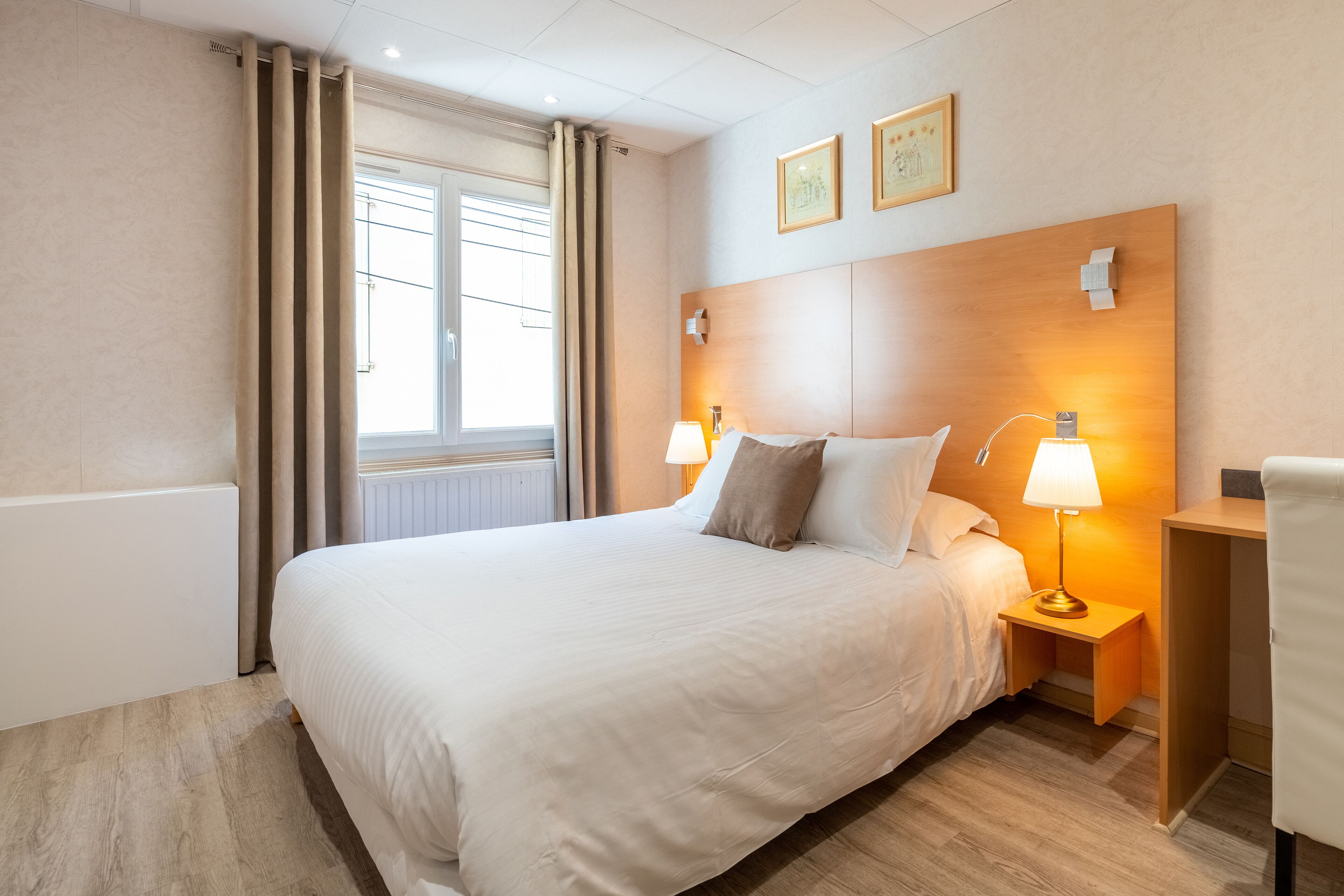 Habitación de hotel con una cama grande, dos lámparas de noche, un cabecero de madera y una mesita de noche pequeña de madera.