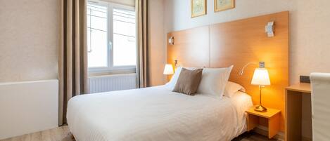 Habitación de hotel con una cama grande, dos lámparas de noche, un cabecero de madera y una mesita de noche pequeña de madera.