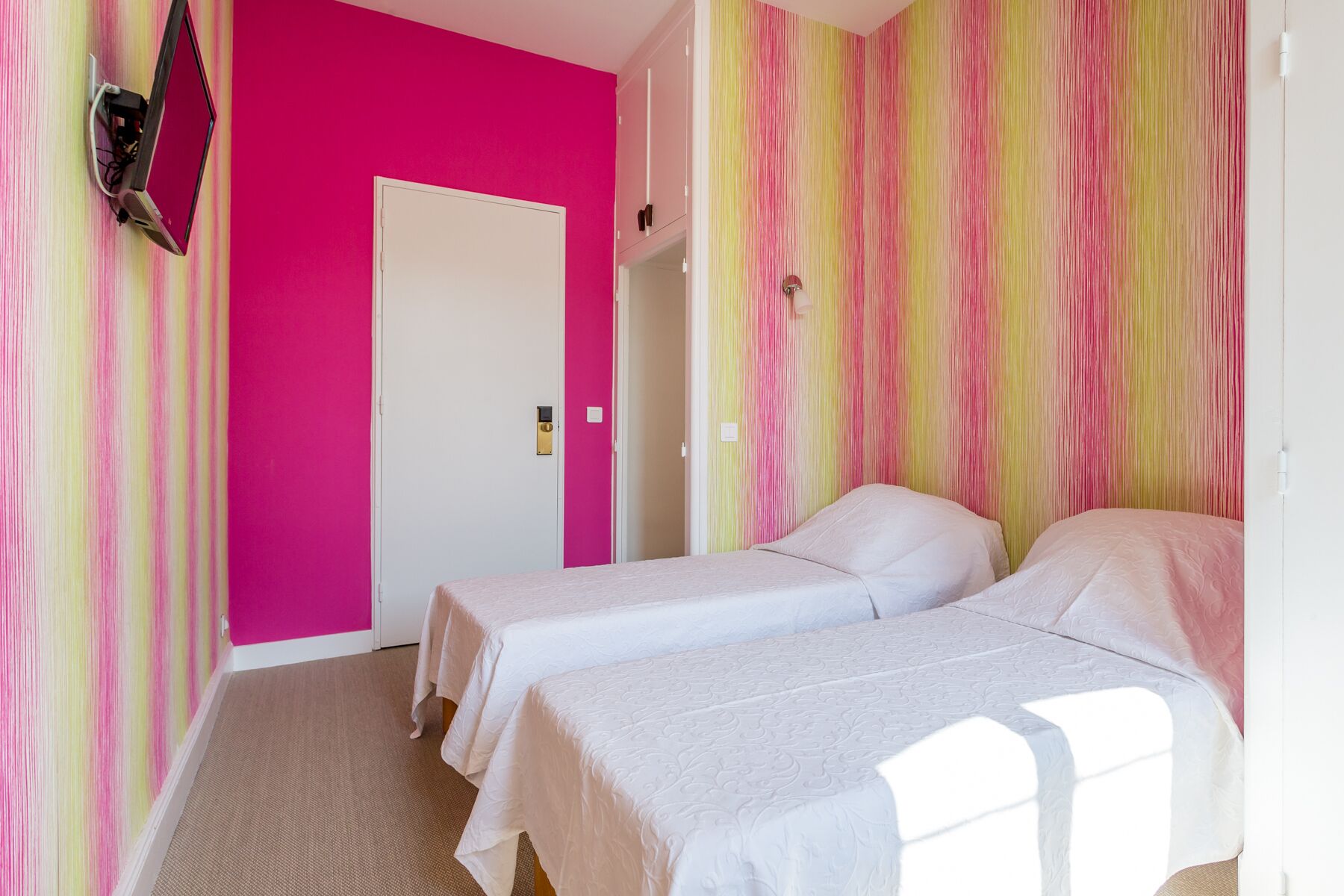 A room with two beds, a door, and a wall with a striped pattern.