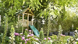 Une cabane en bois avec un toboggan, située dans un jardin agrémenté de plantes en fleurs.