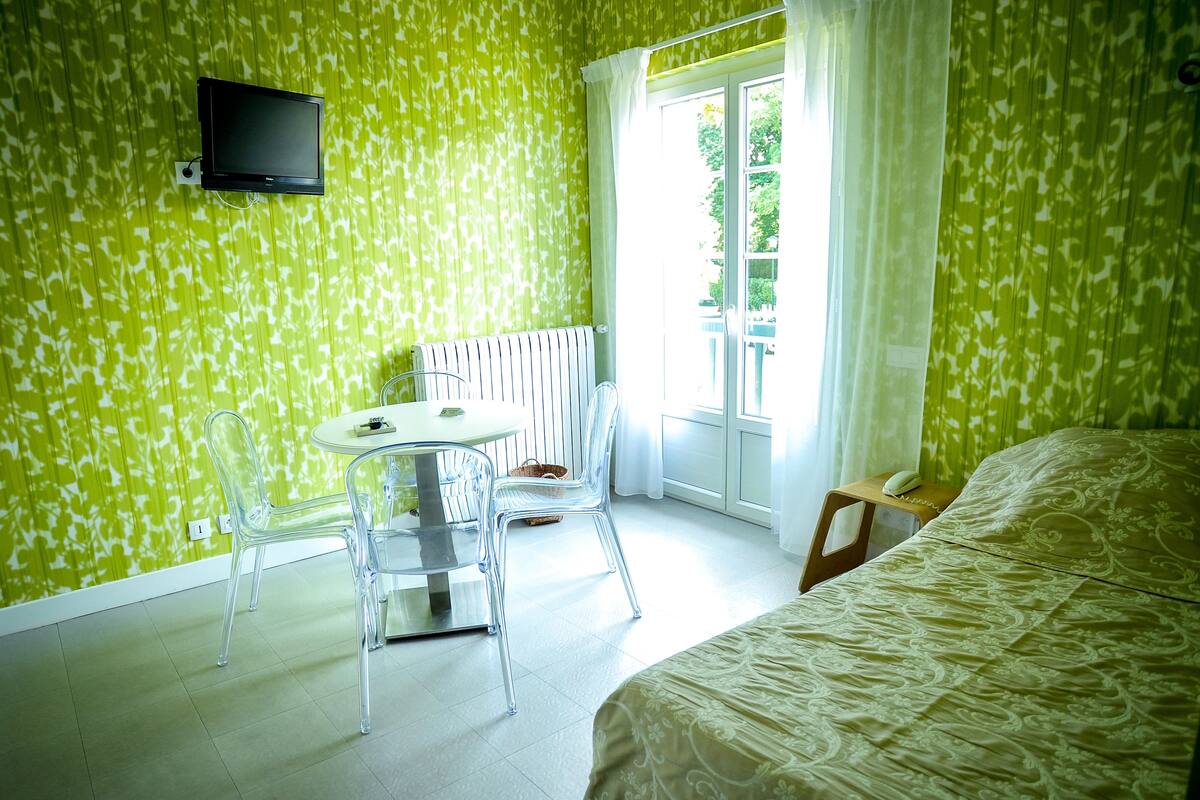 Una habitación con una cama, una mesa con sillas, un radiador y un televisor montado en la pared.