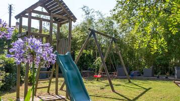 A wooden play structure with a slide and swings in a grassy backyard.