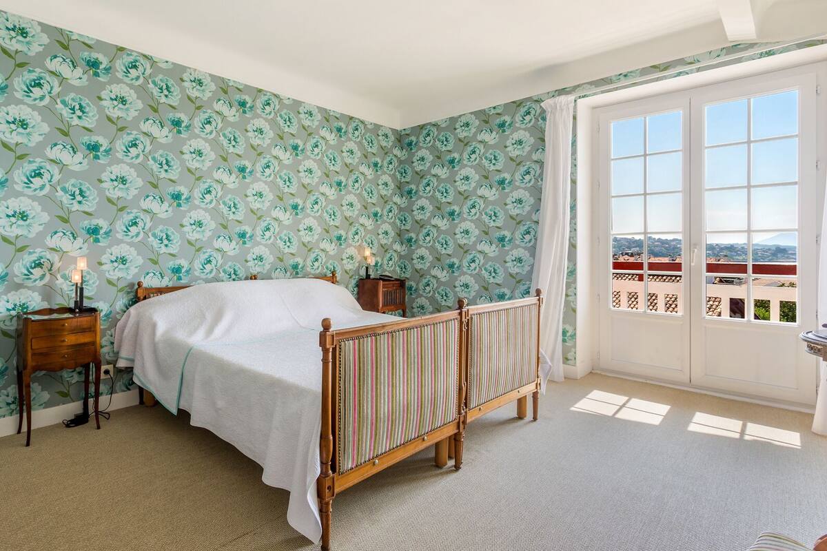 Un dormitorio con una cama, una mesita de noche, una lámpara, una ventana con vistas y una puerta.