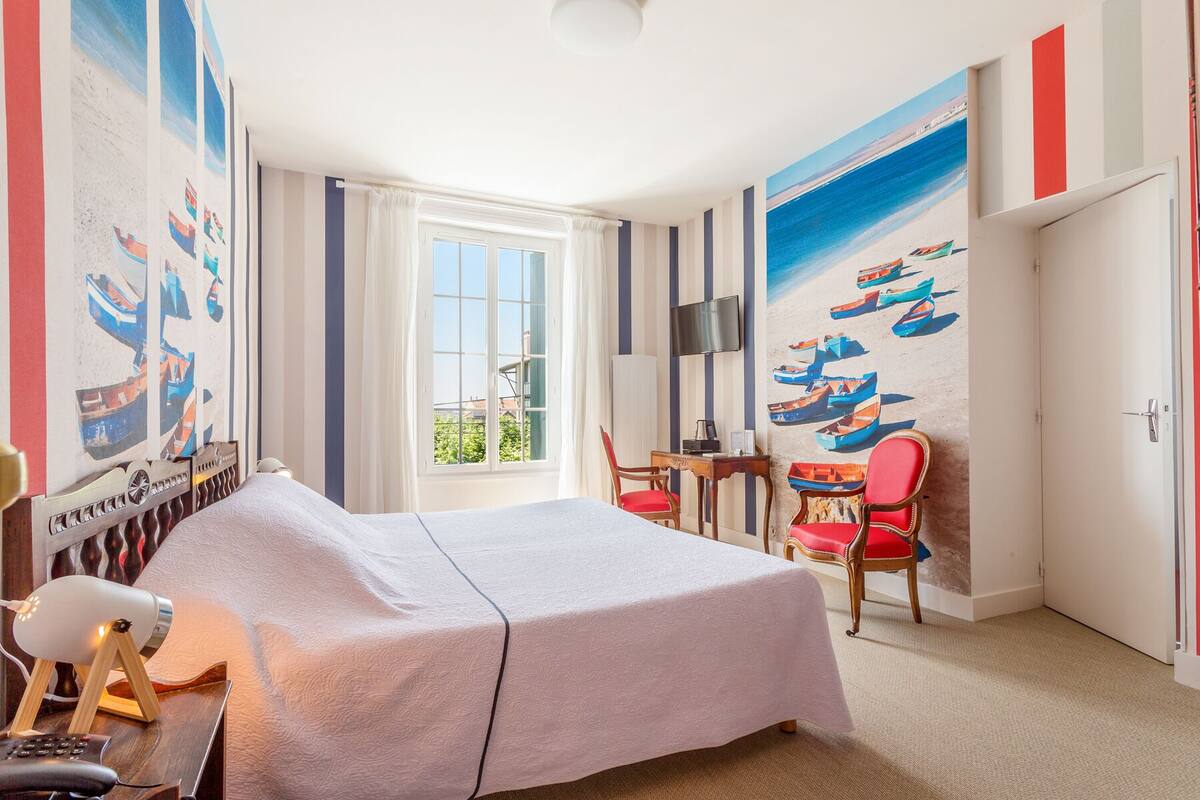 Habitación de hotel con una cama, un escritorio con silla, un televisor y un cuadro de barcos en la pared.