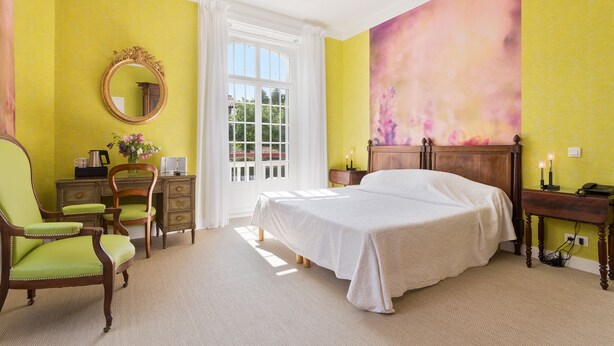 Une chambre à coucher avec un lit, un bureau, une chaise, un miroir et une grande fenêtre.