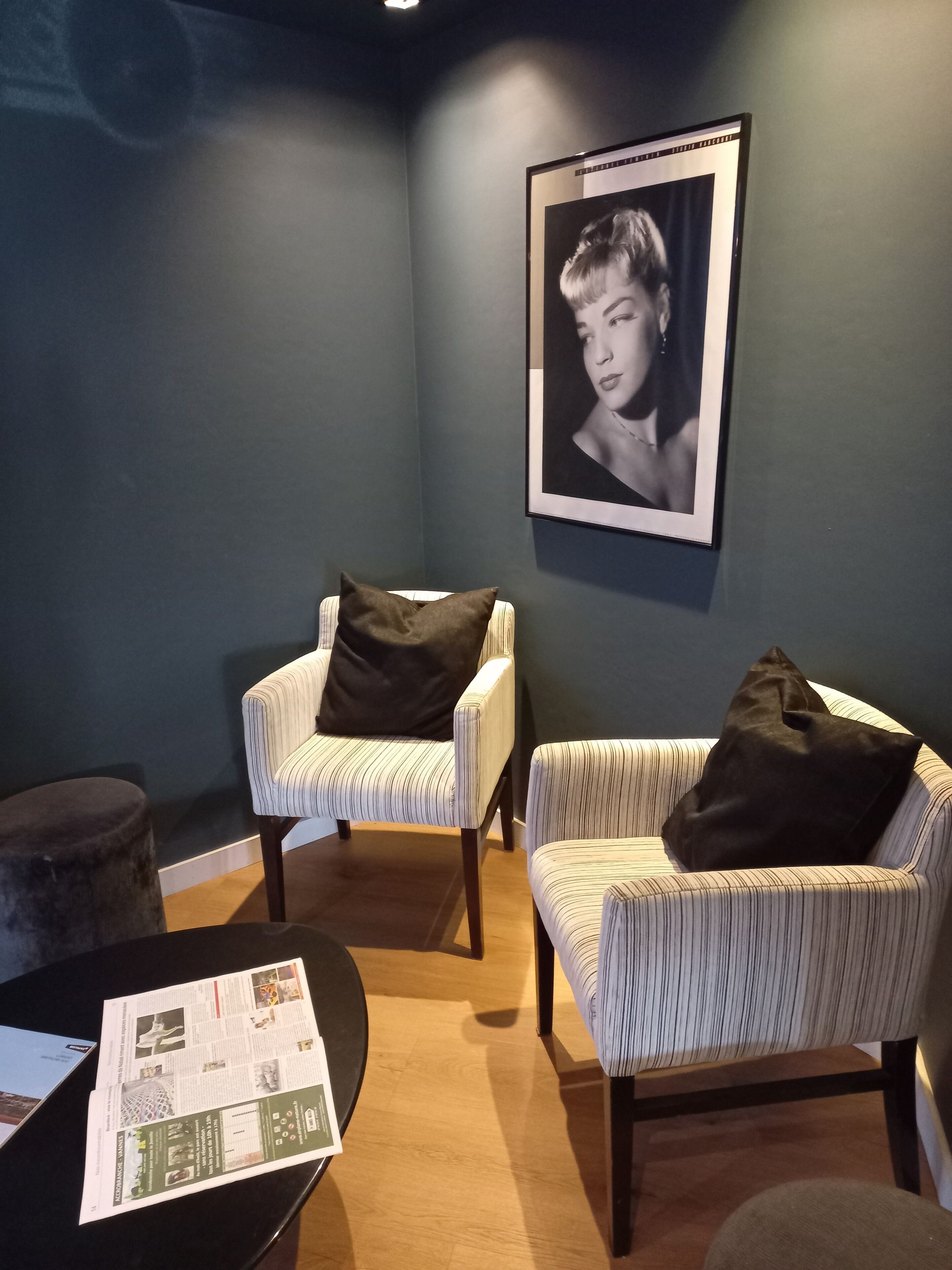 A room with two striped armchairs, a round table with a magazine, and a framed portrait on the wall.