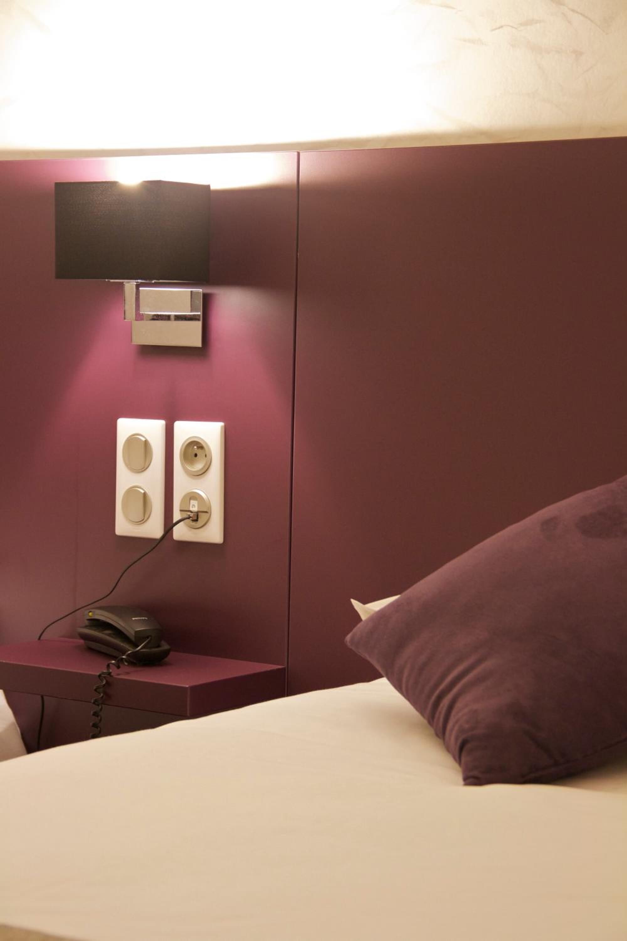Een hotelkamer met een bed, een aan de muur bevestigde televisie, een telefoon op een bijzettafeltje en een stopcontact.