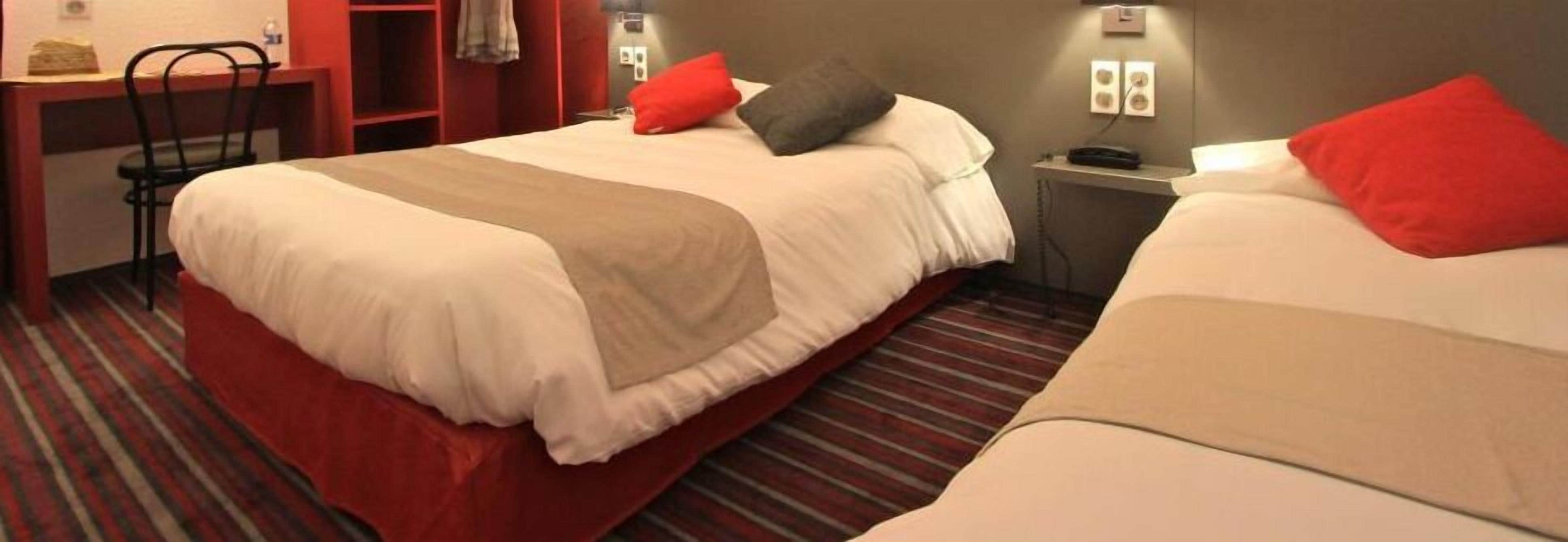 Ett hotellrum med två sängar, var och en med en röd kudde, ett rött nattduksbord med en telefon och en randig matta.