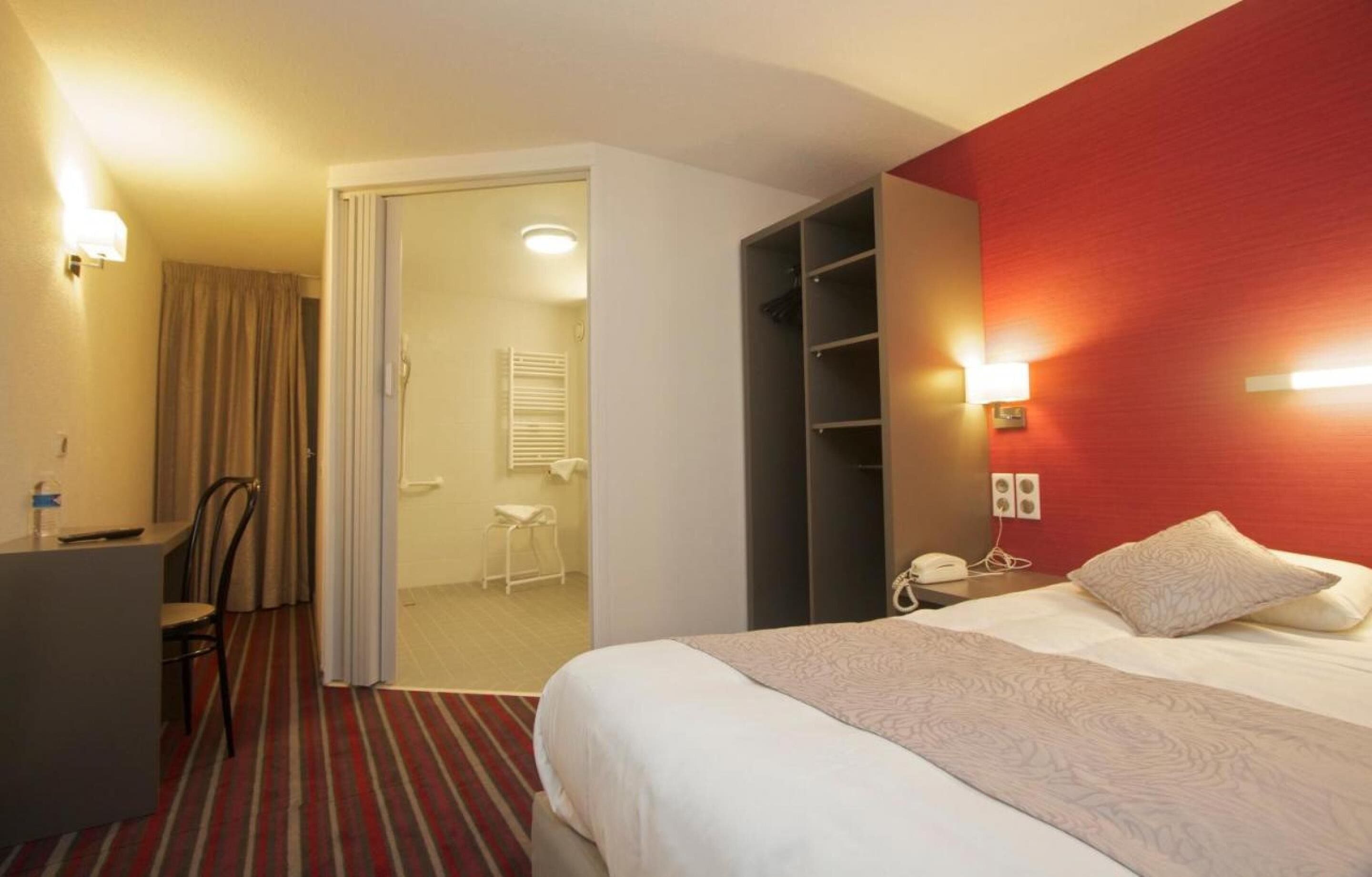 A hotel room with a bed, a desk, a chair, a wardrobe, and a bathroom.