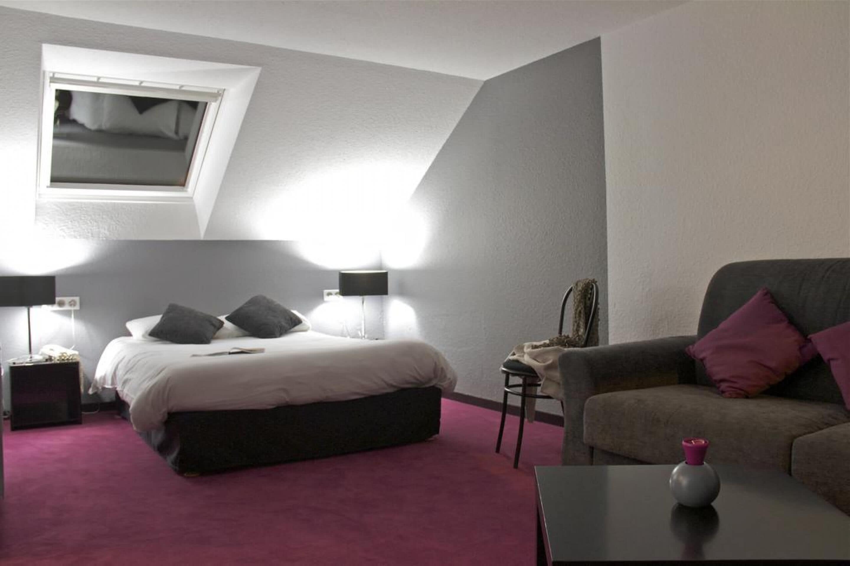A bedroom with a bed, a chair, a nightstand, a lamp, a small table, and a window.