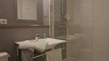 Un baño con ducha de vidrio, un lavamanos con toalla y un espejo sobre él.