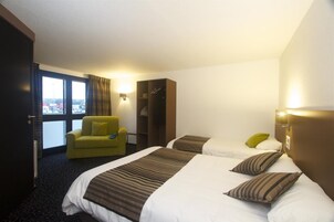 Habitación de hotel con dos camas, un sillón amarillo, un armario y vistas de la ciudad.