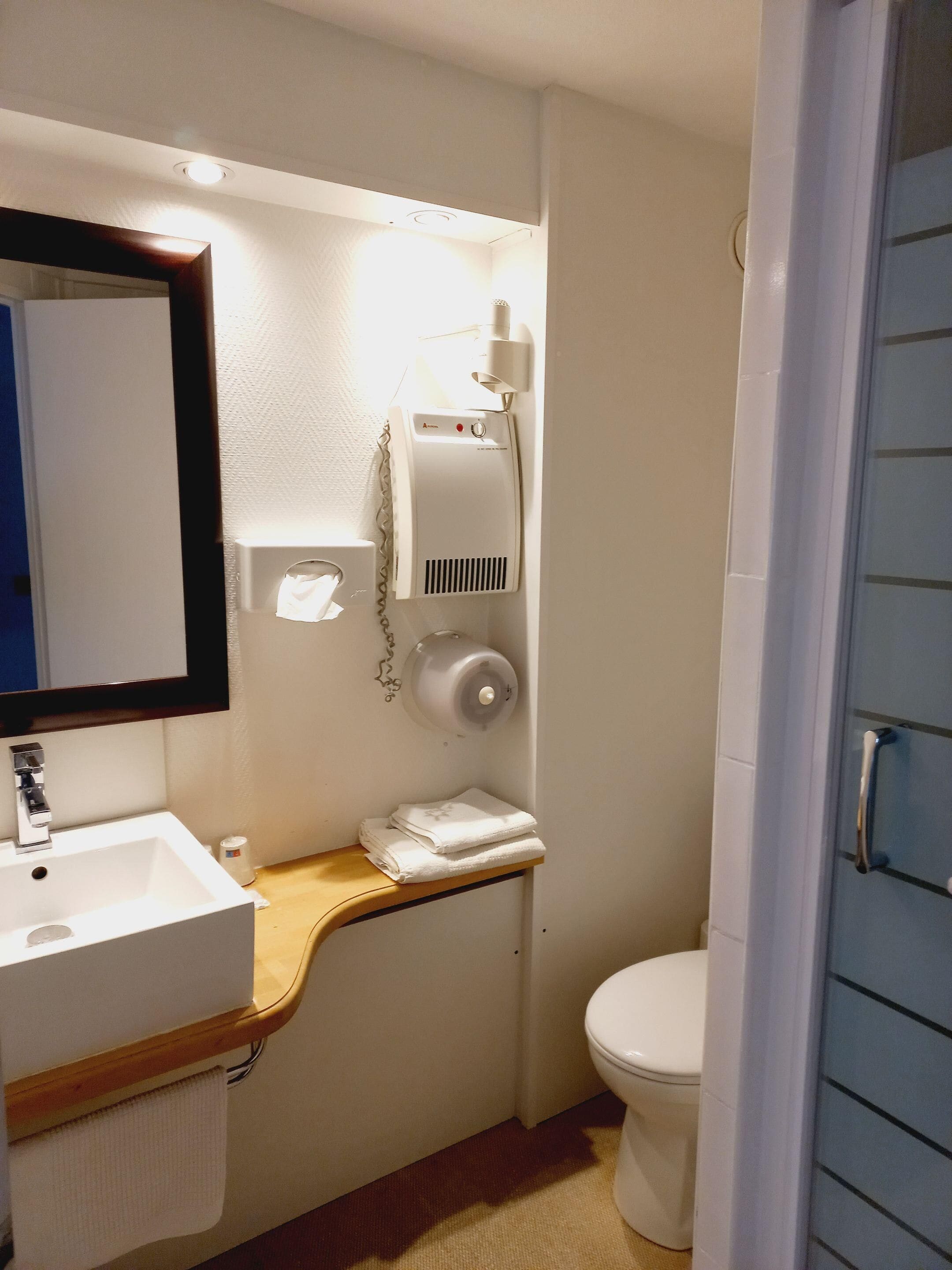 Un baño pequeño con lavamanos, espejo, dispensador de toallas y retrete.
