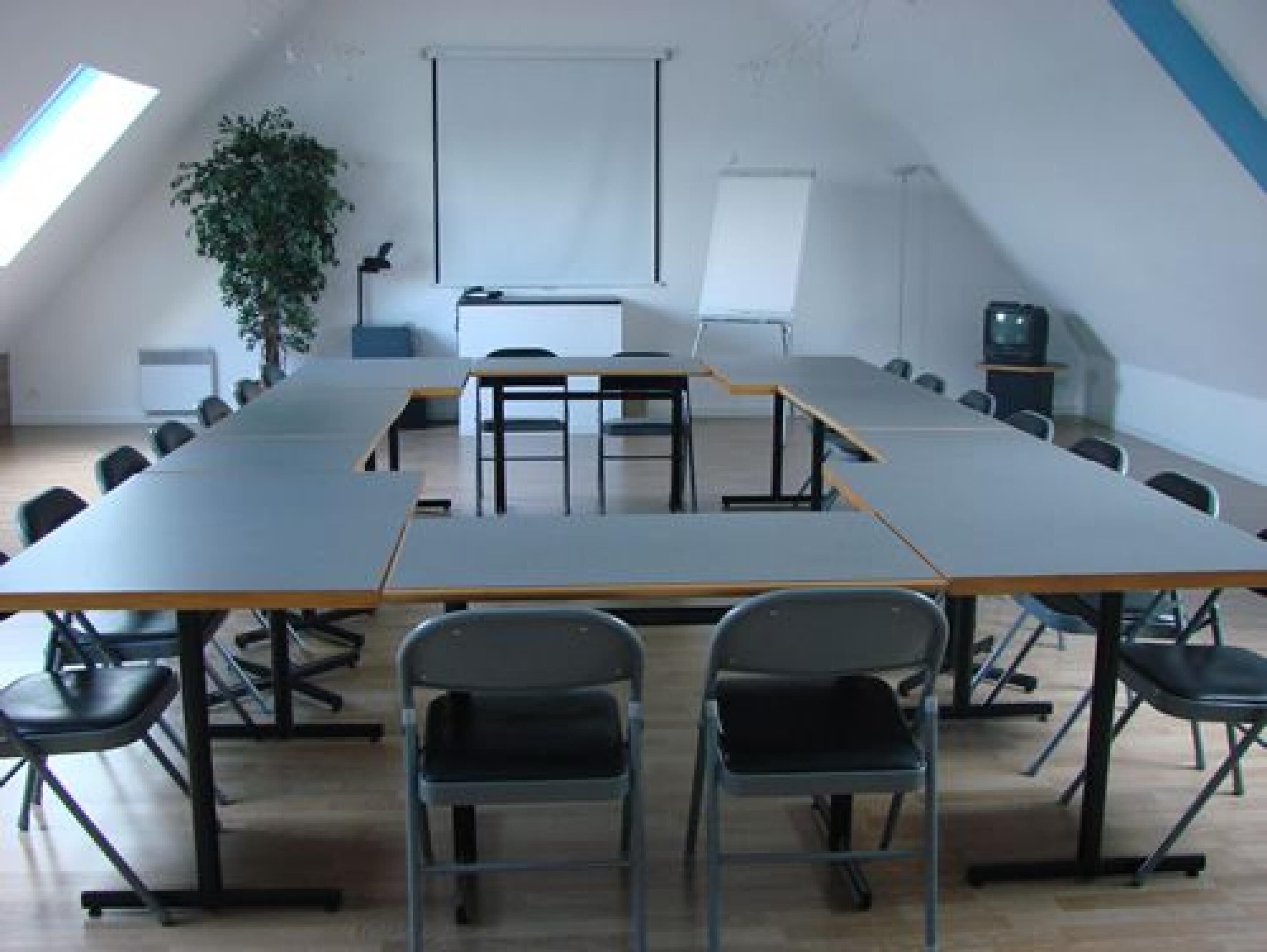 Ein Konferenzraum mit einem langen Tisch, Stühlen, einer Projektionsleinwand und einer Whiteboard-Wand.