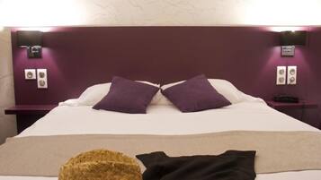 A hotel room with a large bed, purple headboard, and two bedside tables with lamps.