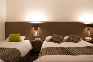 Quarto de hotel com duas camas, cada uma com travesseiro e mesa de cabeceira com telefone.