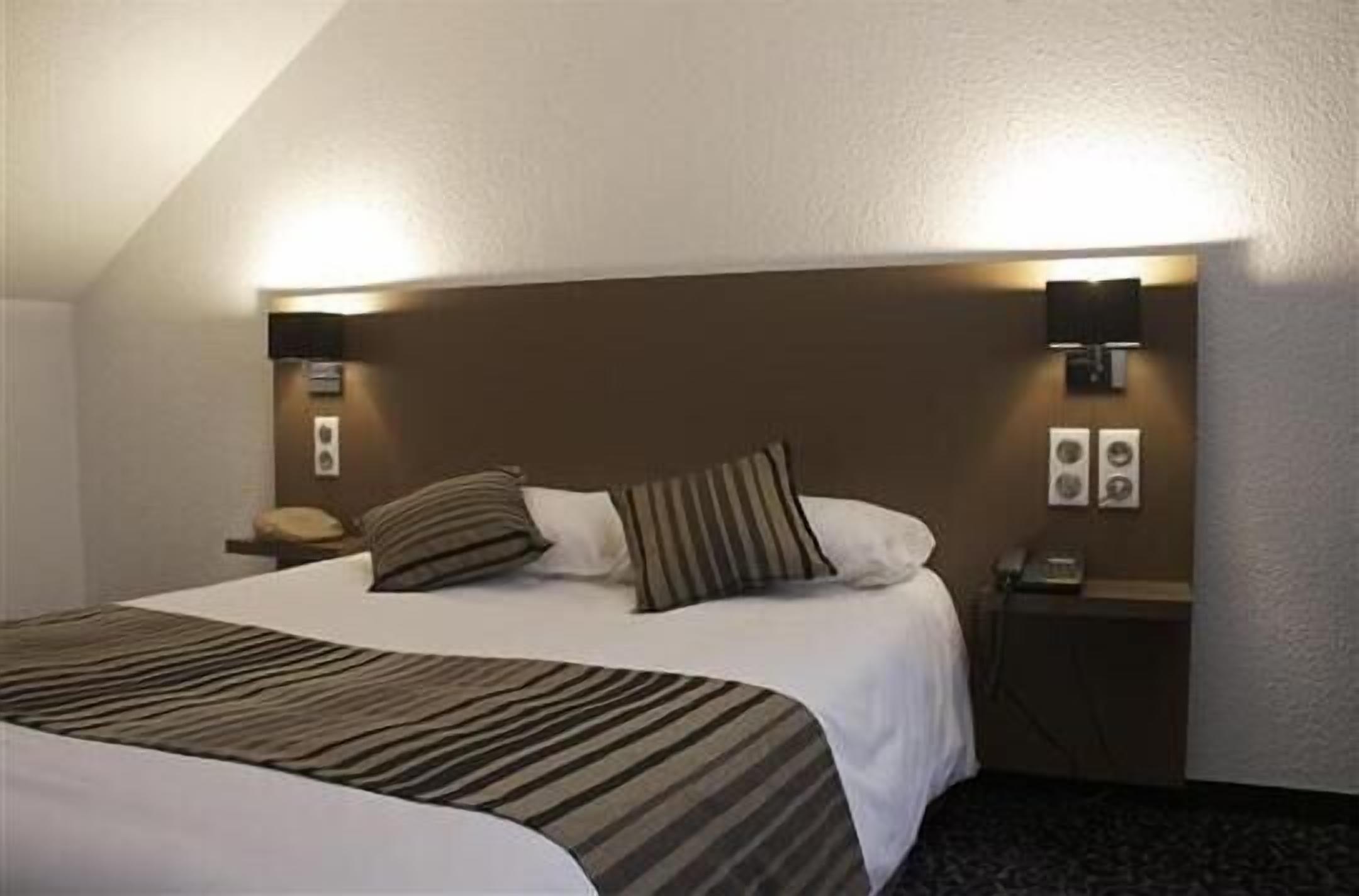 A hotel room with a large bed, two bedside lamps, a nightstand, and a wall-mounted phone.