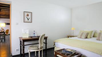 A hotel room with a bed, a desk with a chair, a bedside table, a framed picture on the wall, and a lamp on the desk.