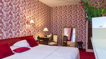 Une chambre d’hôtel avec un lit, un bureau doté d’une lampe, une chaise, un miroir et une moquette rouge.