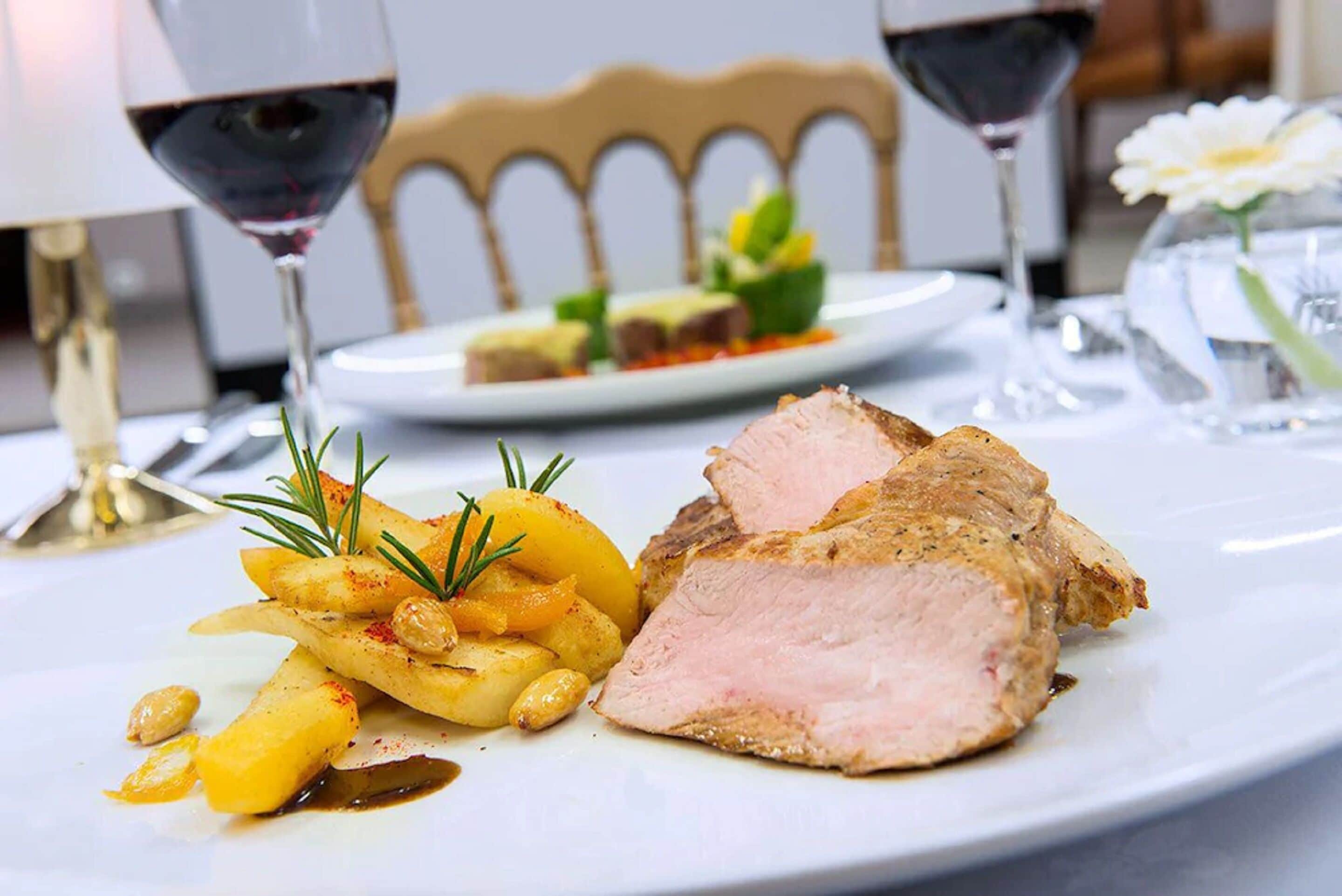 A plate of sliced meat with potatoes and a sprig of rosemary.