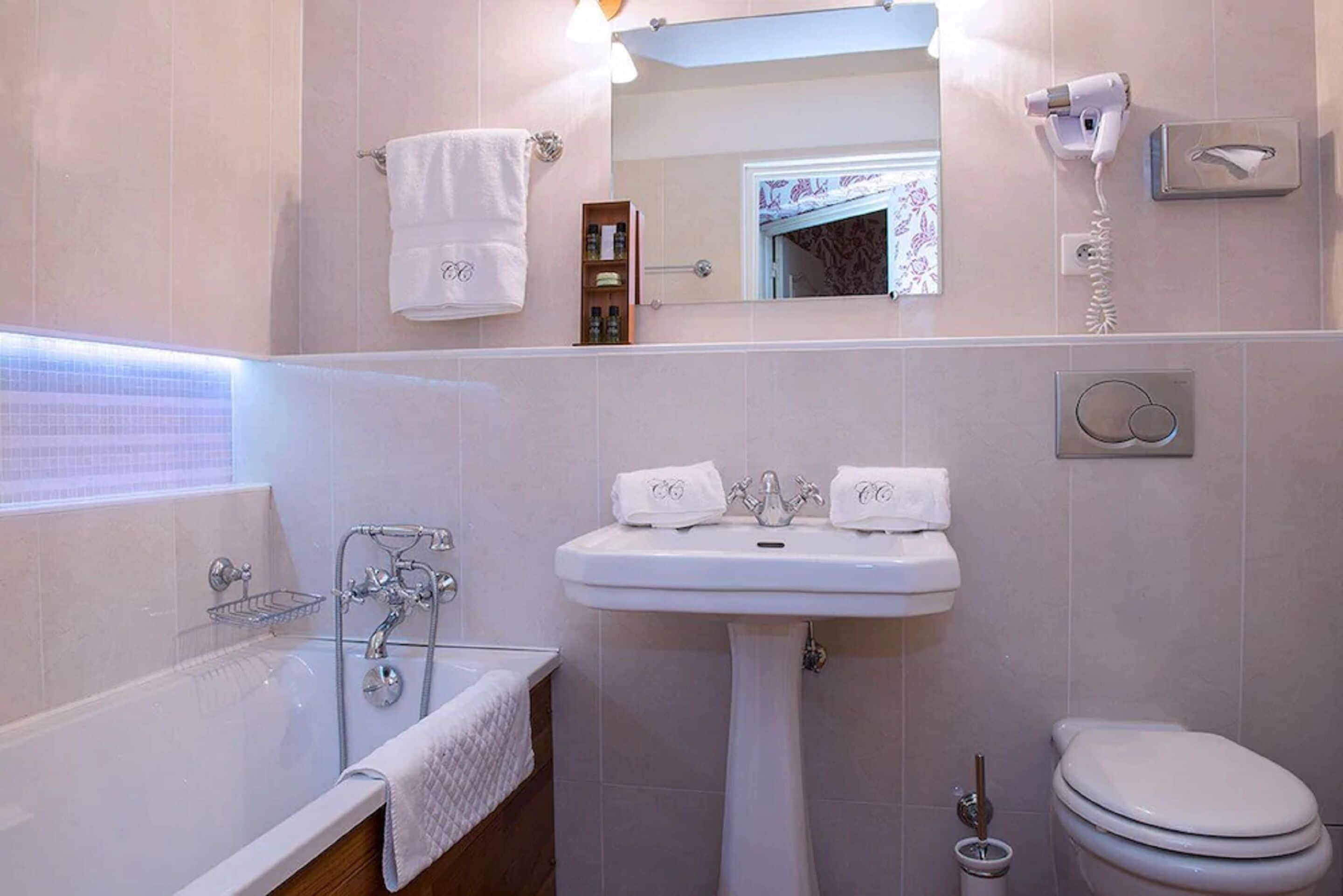 Une salle de bain avec une baignoire, un lavabo à deux robinets, des toilettes et un porte-serviettes.