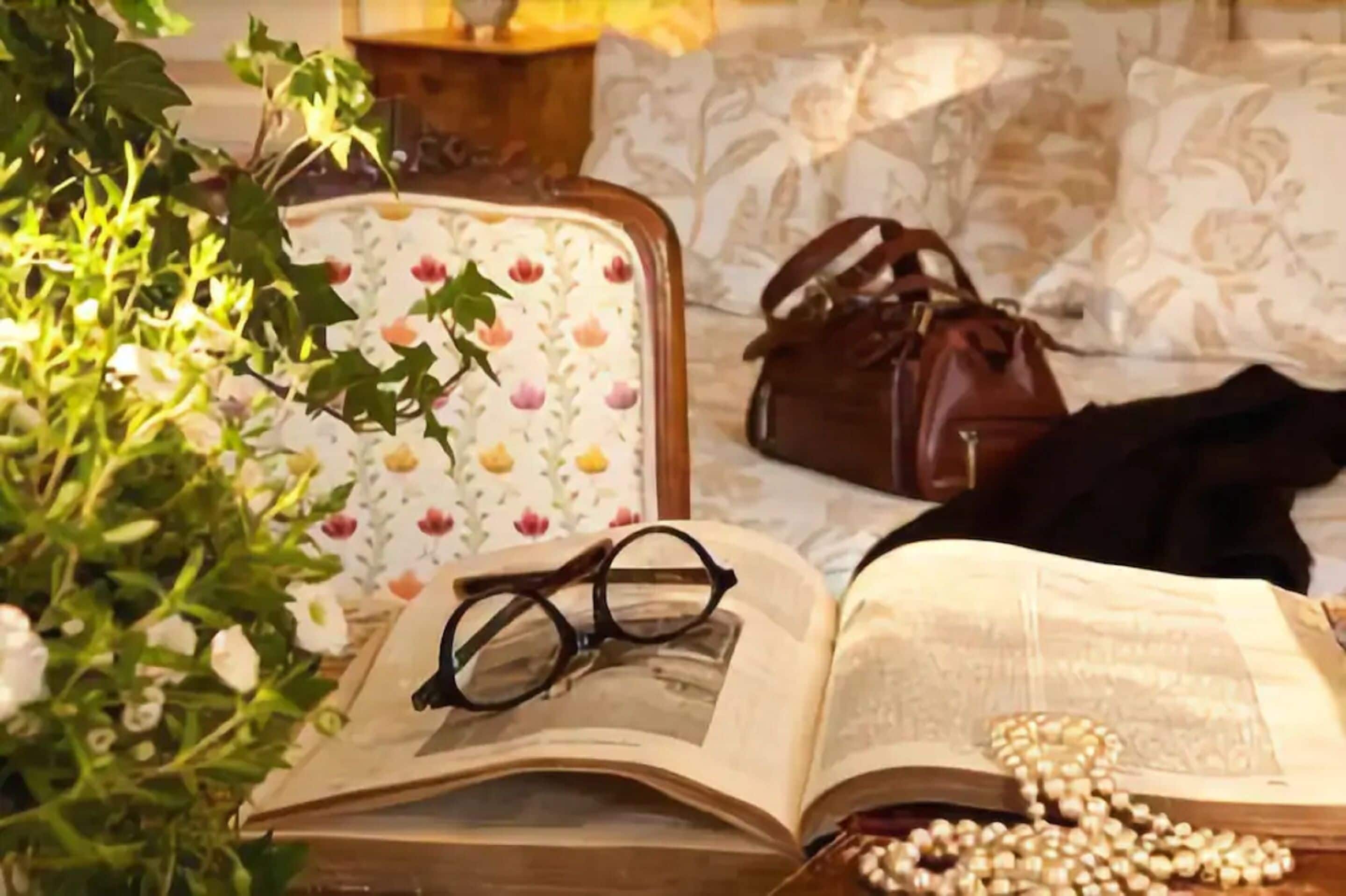 A room with a floral-patterned chair, a brown handbag, a pair of glasses, and a rosary on an open book.