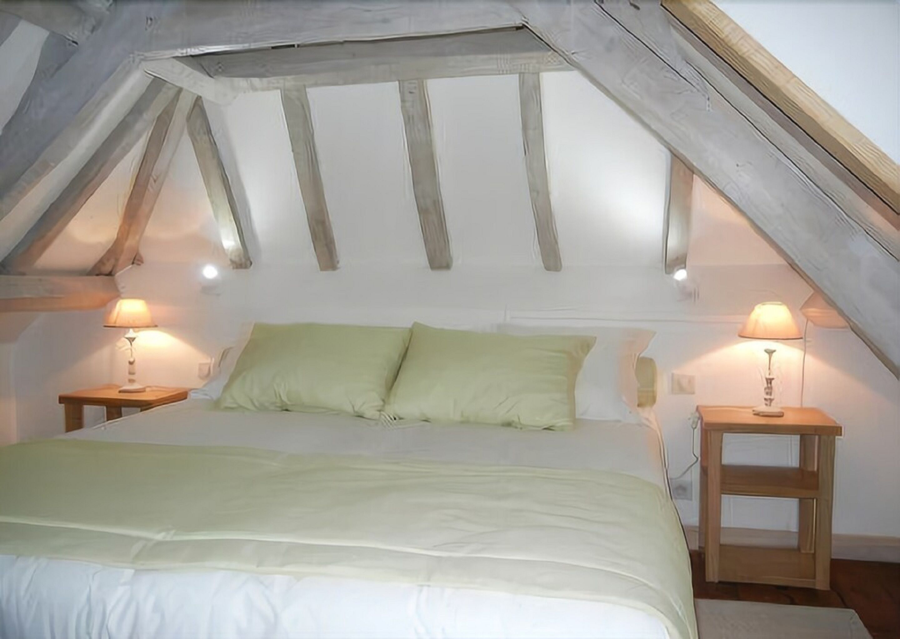 A bedroom with a sloped ceiling, a bed with green bedding, two bedside lamps, and wooden nightstands.