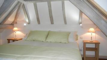 A bedroom with a sloped ceiling, a bed with green bedding, two bedside lamps, and wooden nightstands.
