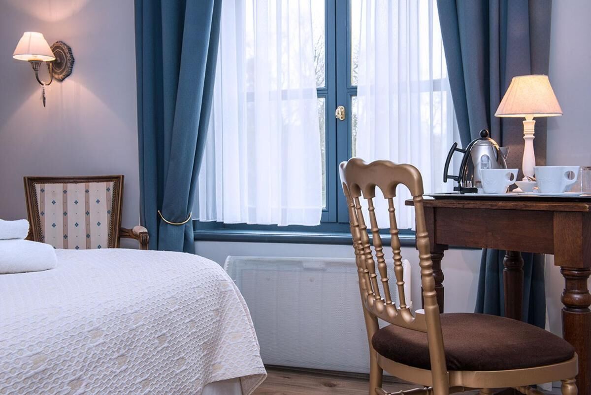 Een hotelkamer met een bed, een houten stoel, een tafel met waterkoker, bekers en een lamp.