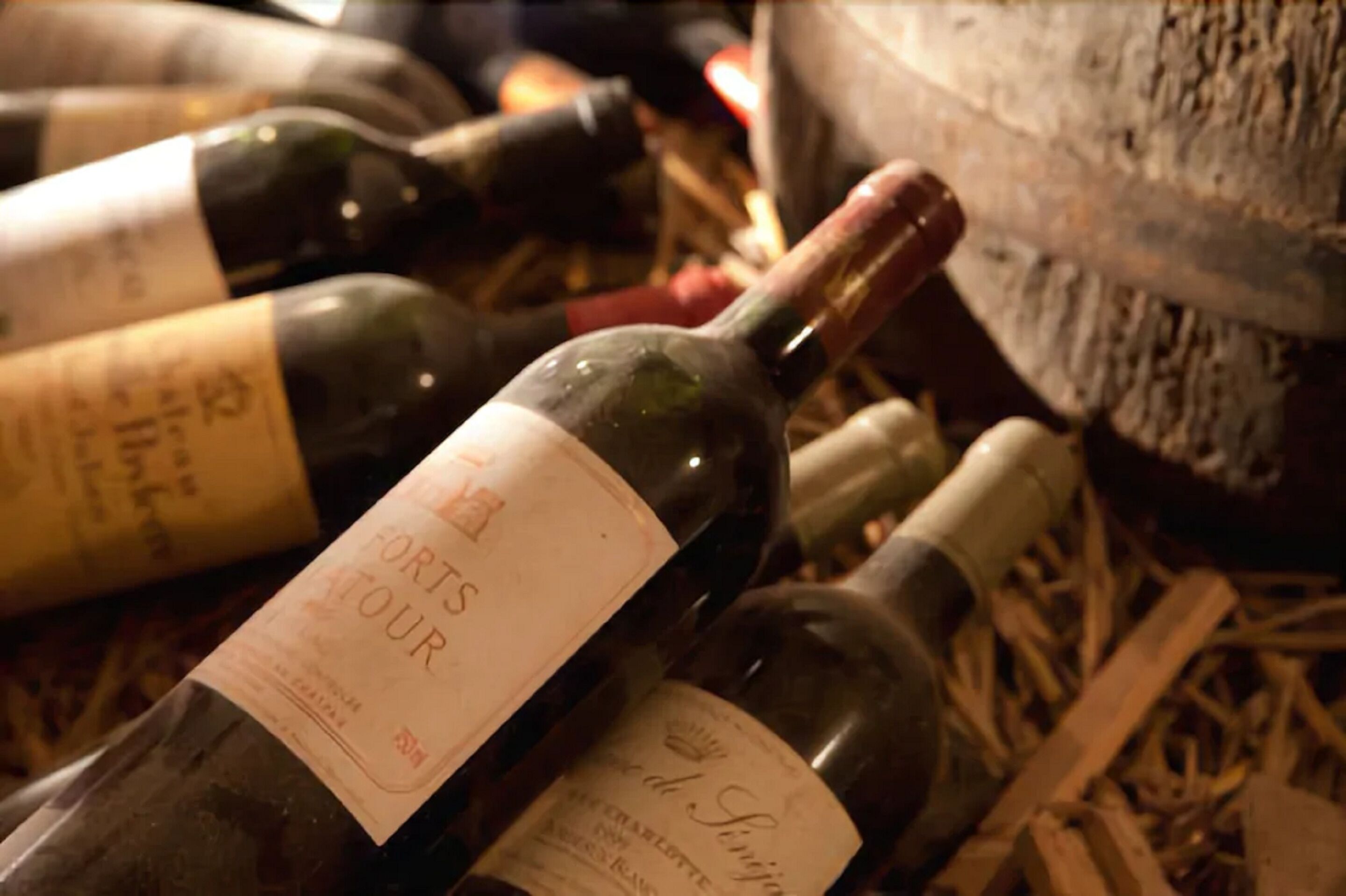 Varias botellas de vino con etiquetas, sobre una superficie cubierta de material similar al heno.