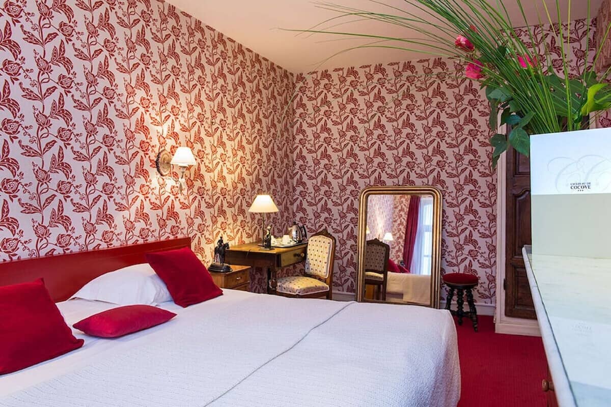 A hotel room with a bed, a desk, a chair, a mirror, and a red carpet.