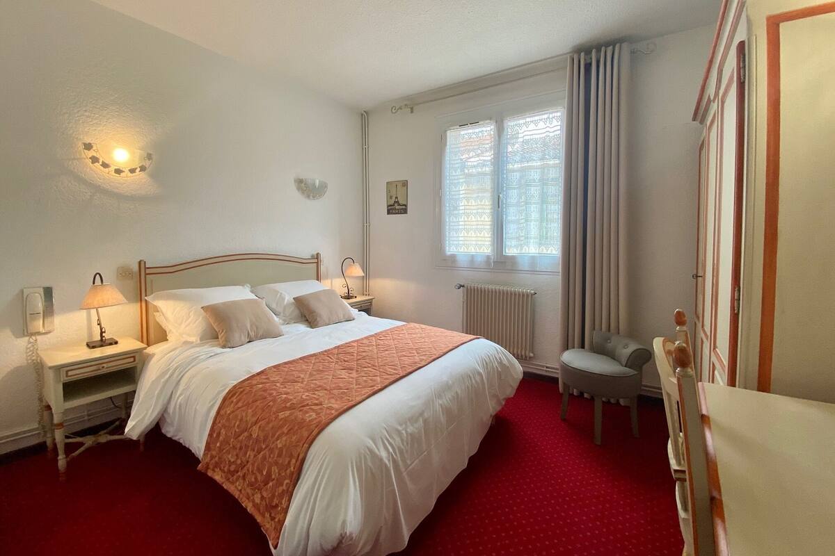 Une chambre bien rangée, avec un lit, des tables de chevet, une chaise et une fenêtre avec des rideaux.