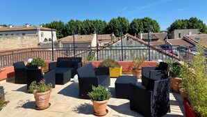 Una terraza en la azotea con mobiliario de mimbre y plantas en macetas, con vistas a una zona residencial con tejados de teja.