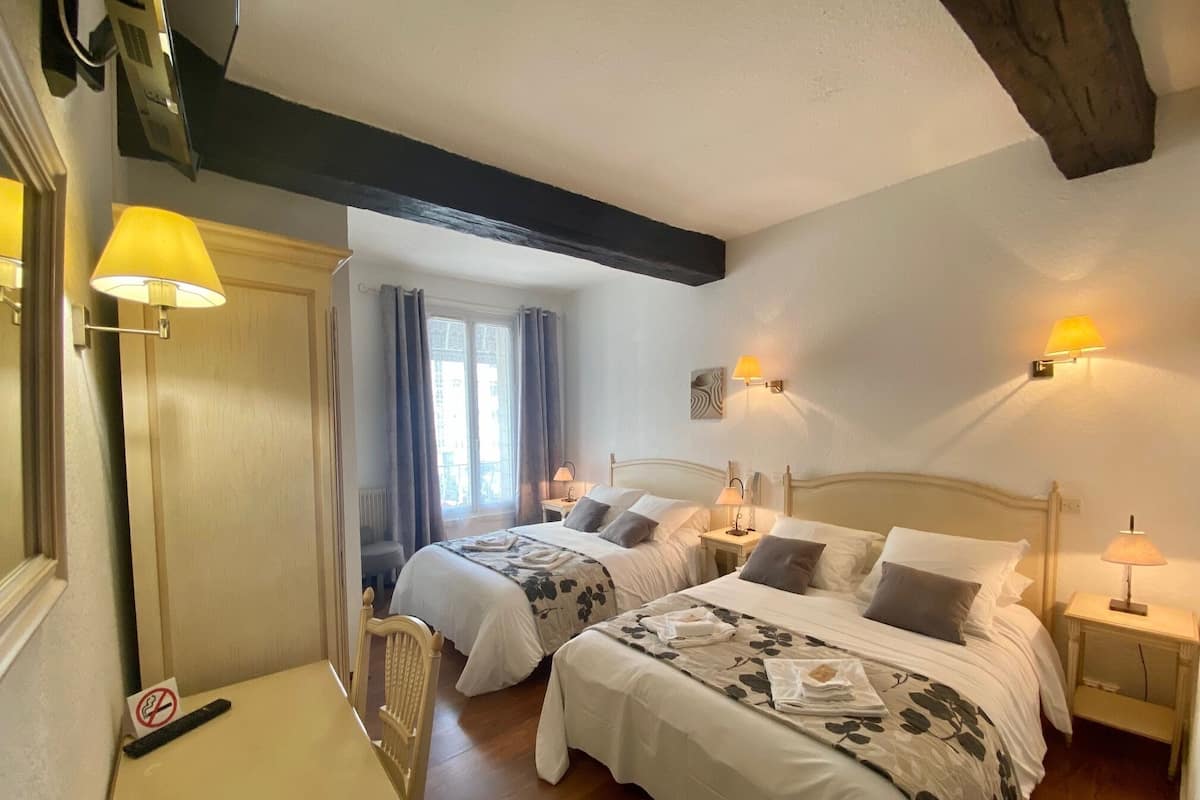 Une chambre d’hôtel avec deux lits, un bureau et une chaise. Il y a deux tables de chevet avec des lampes.