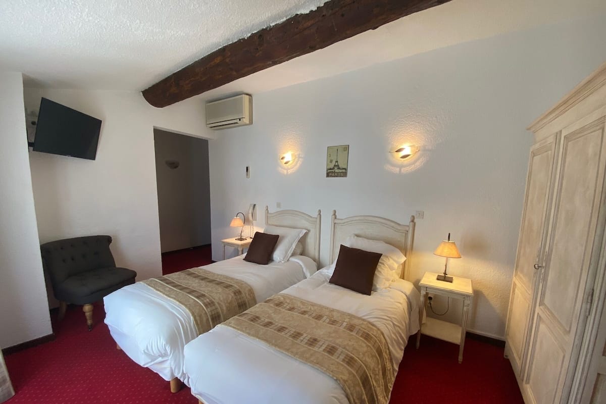 Une chambre d’hôtel avec deux lits, une télévision, une armoire et une moquette rouge.
