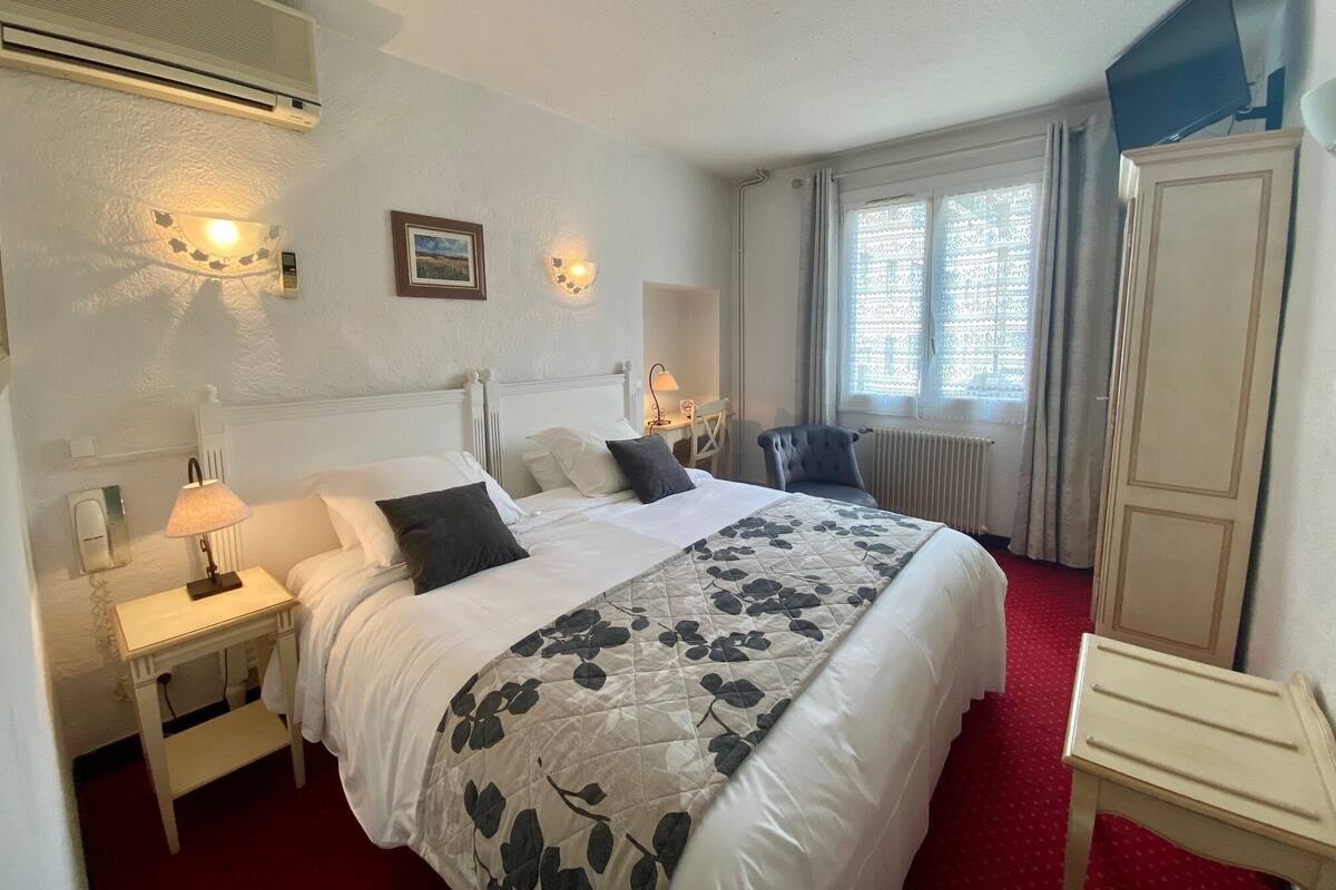 Une chambre d’hôtel comprenant un lit, des tables de chevet, une lampe, une chaise, une armoire et une fenêtre avec des rideaux.