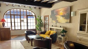 Una sala de estar acogedora con un amplio ventanal arqueado, un cuadro de un atardecer y una planta en maceta.