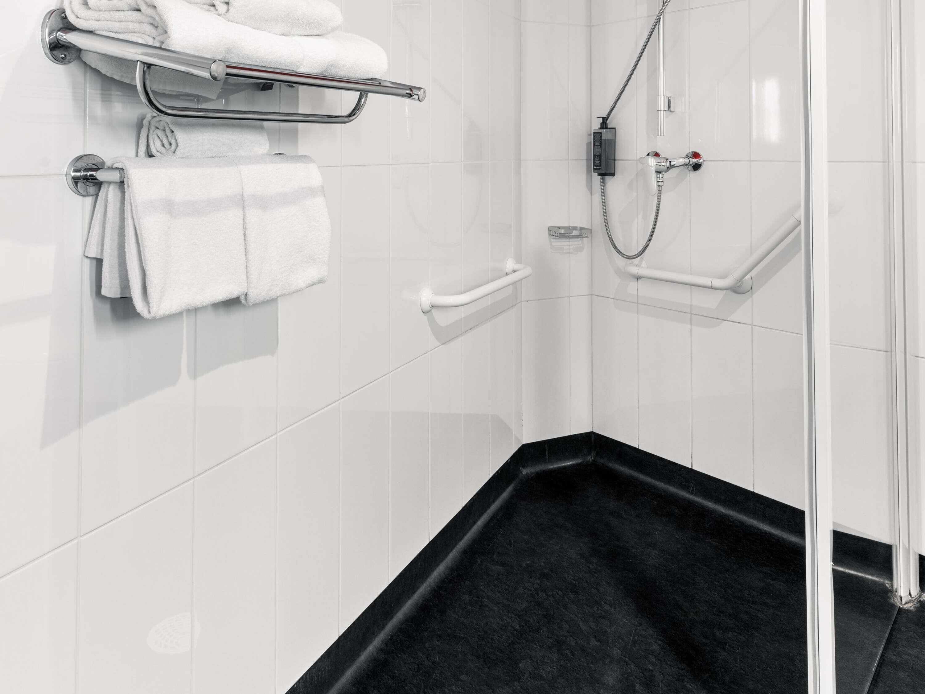 A modern bathroom with white tiled walls, a black bathtub, and a glass shower enclosure.