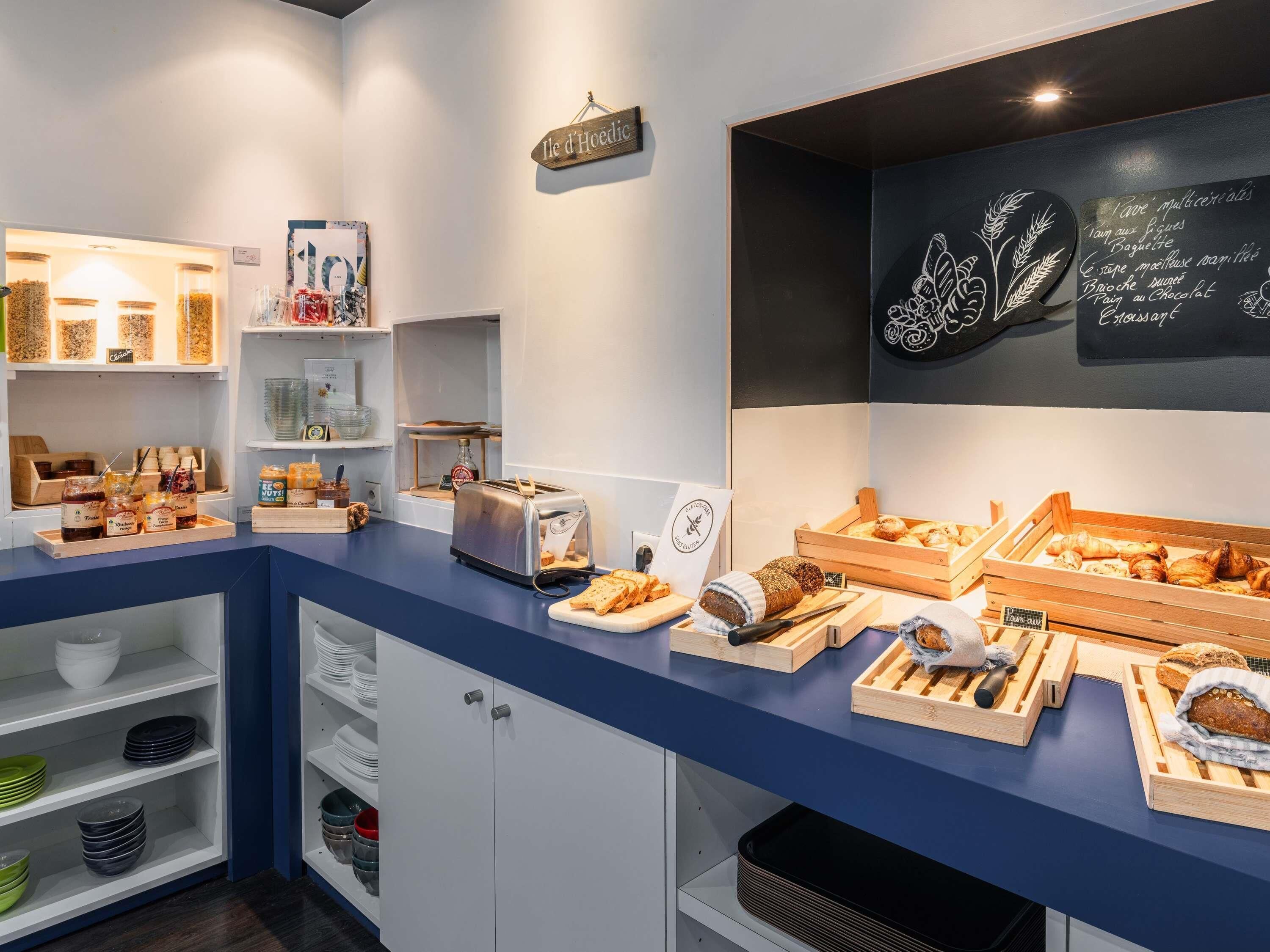 Eine Theke in einer Bäckerei mit verschiedenen Backwaren und einer Kreidetafel, die Produkte wie Baguettes und Croissants auflistet.
