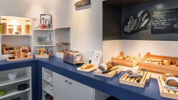 Eine Theke in einer Bäckerei mit verschiedenen Backwaren und einer Kreidetafel, die Produkte wie Baguettes und Croissants auflistet.