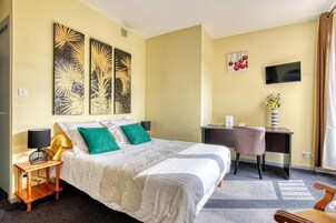 Una camera d'albergo con un letto, una scrivania, una sedia, un televisore e opere d'arte alle pareti.