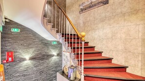 Eine Treppe mit roten Teppichstufen, einem Holnänder und einer an der Wand befestigten Leuchte.