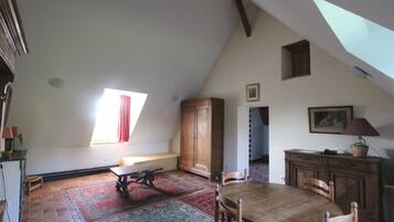 A spacious attic room with a large wooden dining table, a bench, and a view of the sky through a skylight.