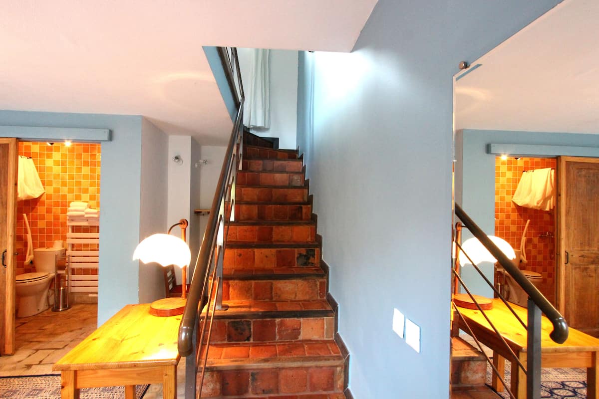 Un escalier avec des marches recouvertes de bois, menant à une pièce dont le sol est carrelé et qui contient une table en bois.