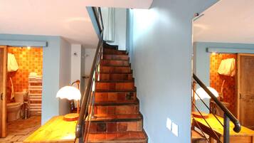 A staircase with a wooden finish, leading to a room with a tiled floor and a wooden table.