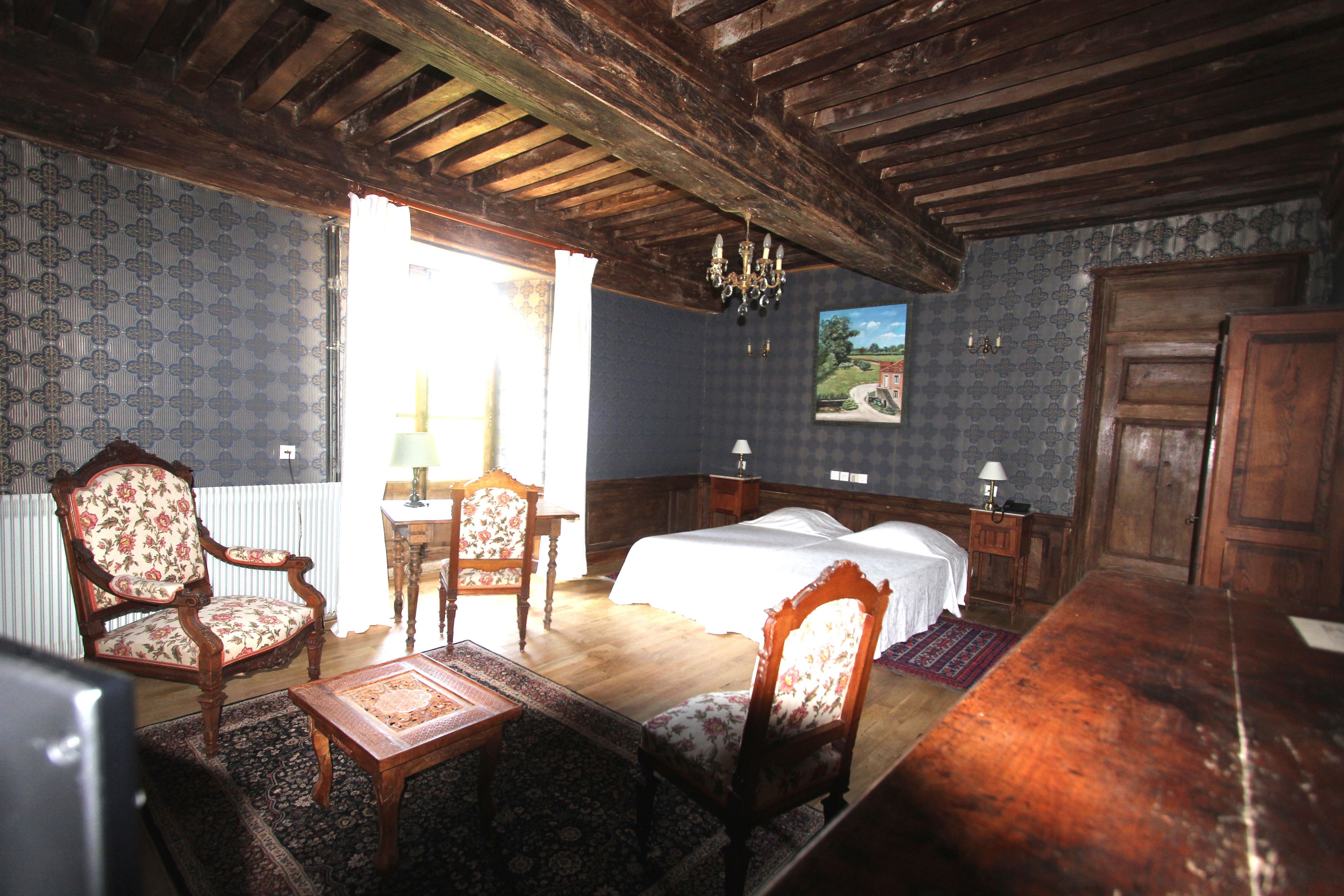 Une pièce avec un plafond en bois, un lit avec deux oreillers, une chaise, une petite table et une table de chevet avec une lampe.