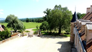 A courtyard with a stone building, a pathway, and a view of a green field and trees. - Château d'Island Avallon Vézelay (Island)